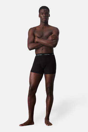 Short de boxers Calvin Calvin Klein, port par un homme avec les bras croisés et pieds nus.
