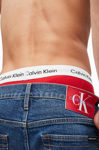 Boxers blancs de Calvin Klein, avec une ceinture rouge et un logo de marque visible sur l'arrière des jeans.