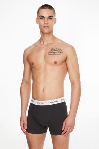 Zwarte boxershorts van Calvin Klein, gedragen door een man met een getatoeëerde borst.
