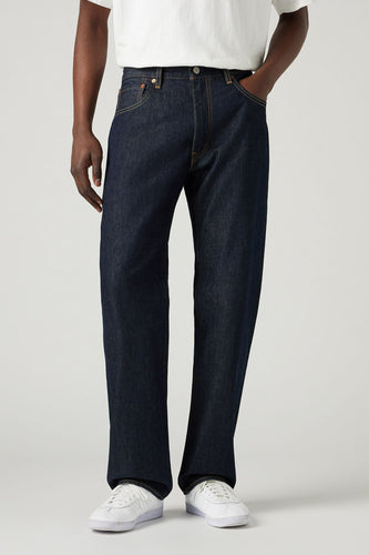 Man in een wit T-shirt en donkerblauwe jeans, met witte sneakers.