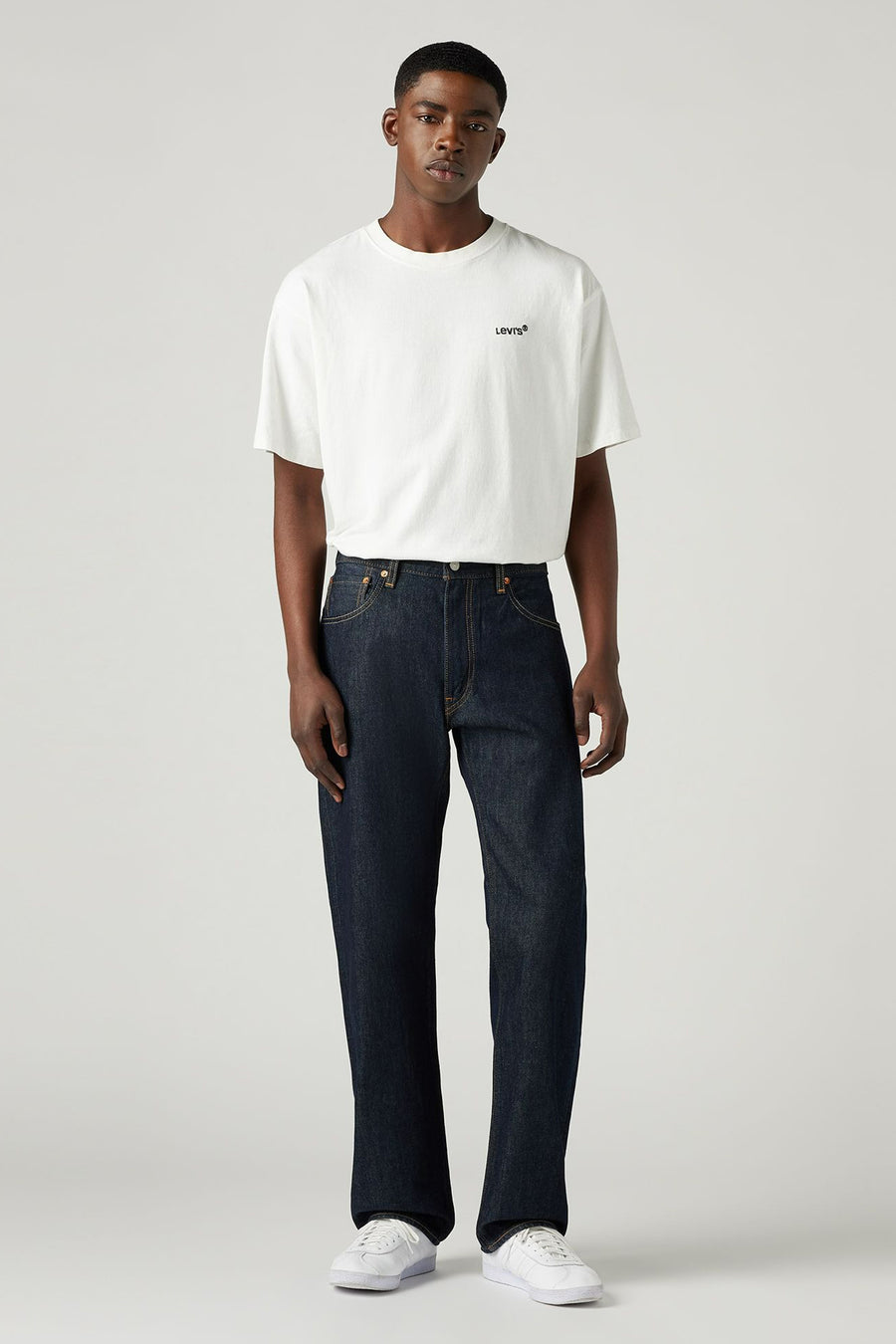 Man met wit T-shirt en donkerblauwe jeans, witte sneakers.