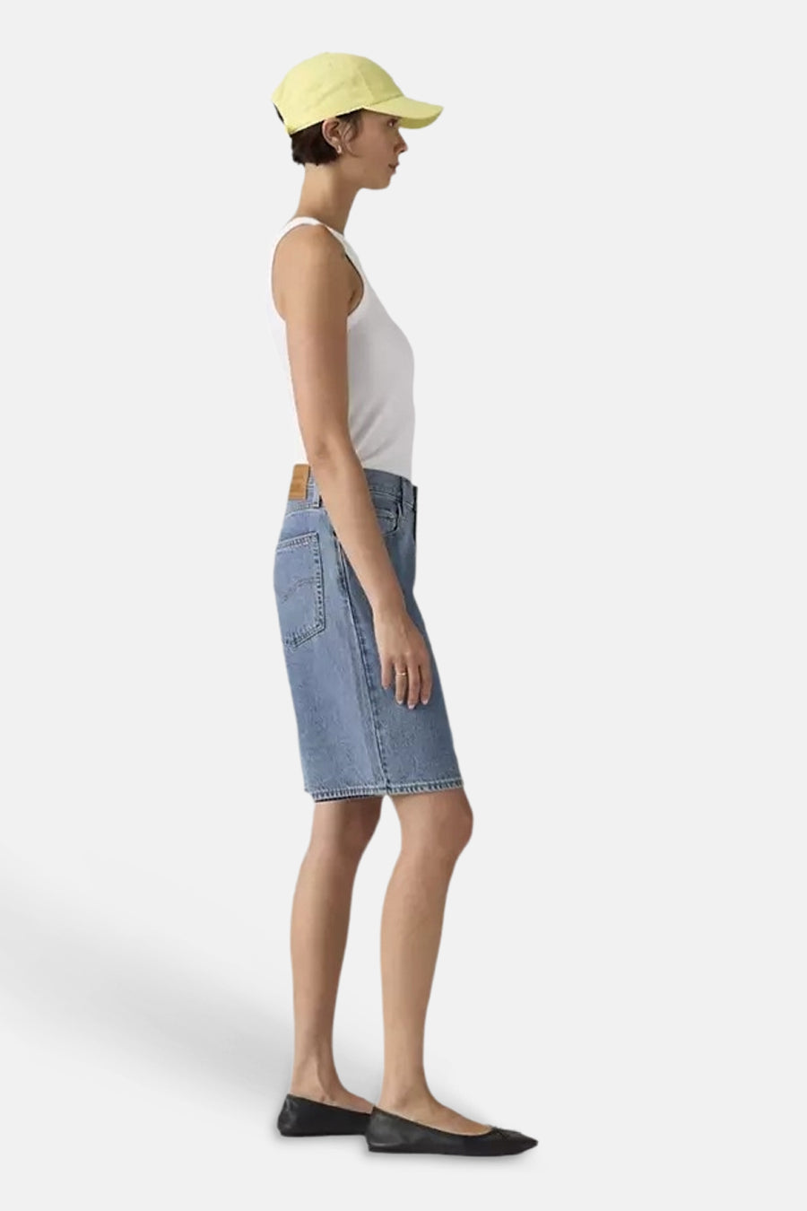 Blauwe mid-lengte denim shorts van Levi's, zijprofiel, met zakken en gelaagde zoom, gedragen met wit tanktop en gele pet