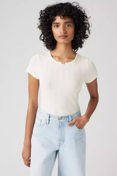 Vrouw met gekrulde haren in een wit ribbelshirt en lichtblauwe jeans.