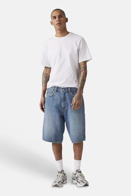 Short en jean bleu clair de Levi's®, porté par un homme en t-shirt blanc et baskets grises, vue de côté.