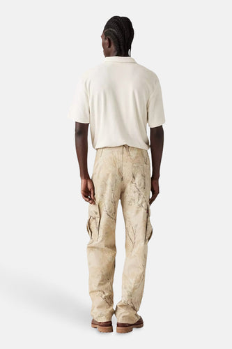 Man van achteren, beige polo, camouflage cargobroek, bruine schoenen, witte achtergrond.