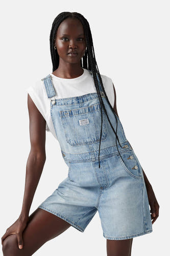 Combinaison de denim bleu clair de Levi's, avec des manches courtes et des bretelles de sac à dos, portée sur un T-shirt blanc, dos.