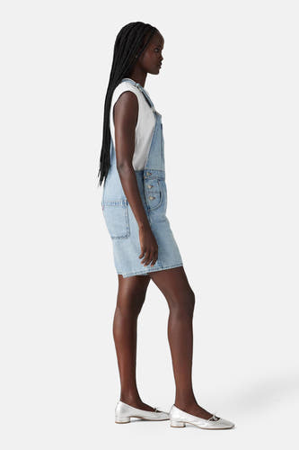 Combinaison en denim bleu clair de Levi's®, avec une chemise blanche et des chaussures argentées.