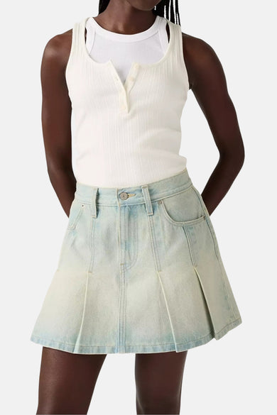 Vrouw in een witte tanktop en een geplooide denim rok.