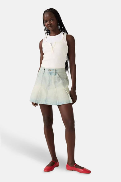 Vrouw draagt witte top, denim rok en rode schoenen.