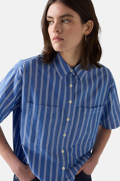 Vrouw in blauw-wit gestreept overhemd met zakken.