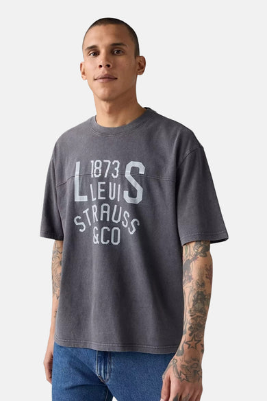 T-shirt gris à manches courtes de Levi's®, avec une impression blanche et porté avec un jean bleu.