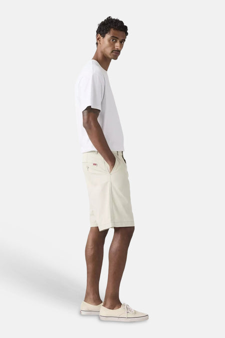Short écru de style chino de Levi's®, avec étiquette rouge sur la poche arrière, porté par un homme avec un T-shirt blanc et des baskets claires.