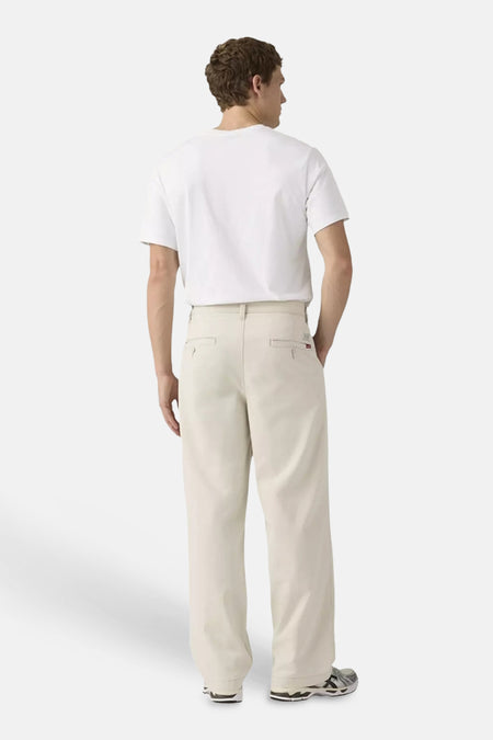 Chino beige à jambes larges de Levi's®, avec poches passepoilées, porté par un homme avec un t-shirt blanc et des baskets.