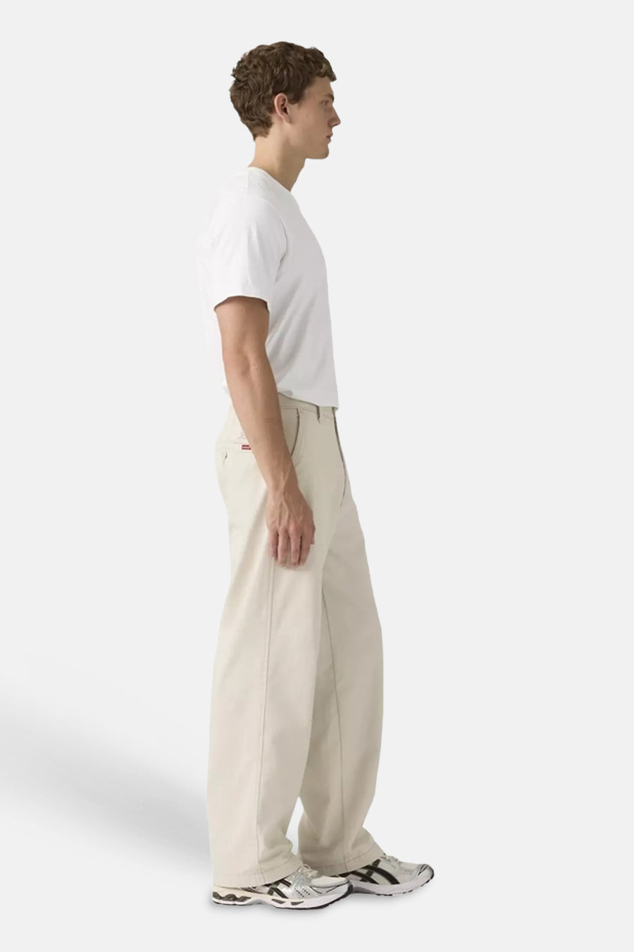 Beige chino van Levi's® met losse pasvorm en rood label, gedragen door een man met wit t-shirt, van opzij.