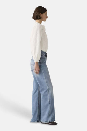 Jean bootcut bleu clair de Levi's® à jambes évasées, porté par un mannequin dans une chemise à pois blancs, en profil latéral.