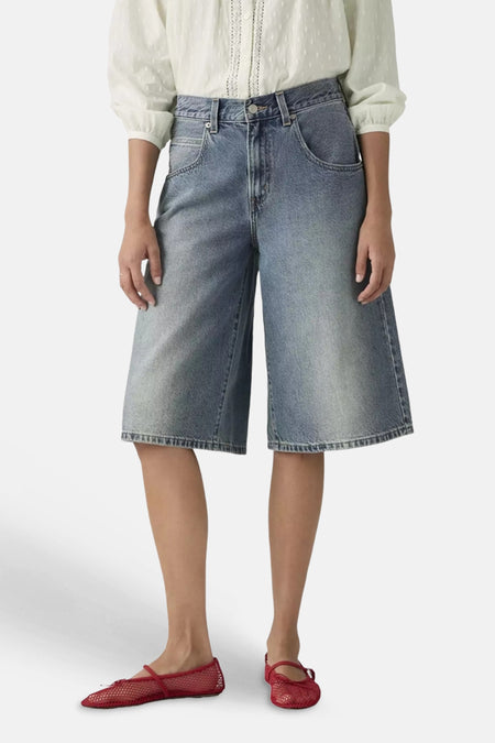 Short en jean bleu clair de Levi's® à jambes larges, avec poches arrière et écusson en cuir, vue arrière, porté avec un chemisier blanc et des ballerines rouges.