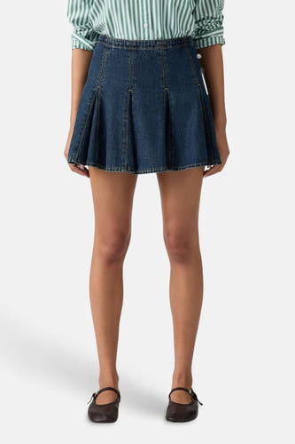 Jupe courte en denim bleu foncé de Levi's® avec détails plissés, portée avec une chemise rayée à l'arrière.