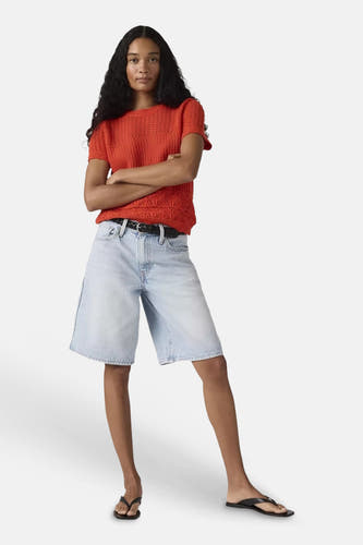 Short en jean bleu clair de Levi's®, porté par un mannequin avec un haut en maille rouge, une ceinture noire et des tongs.