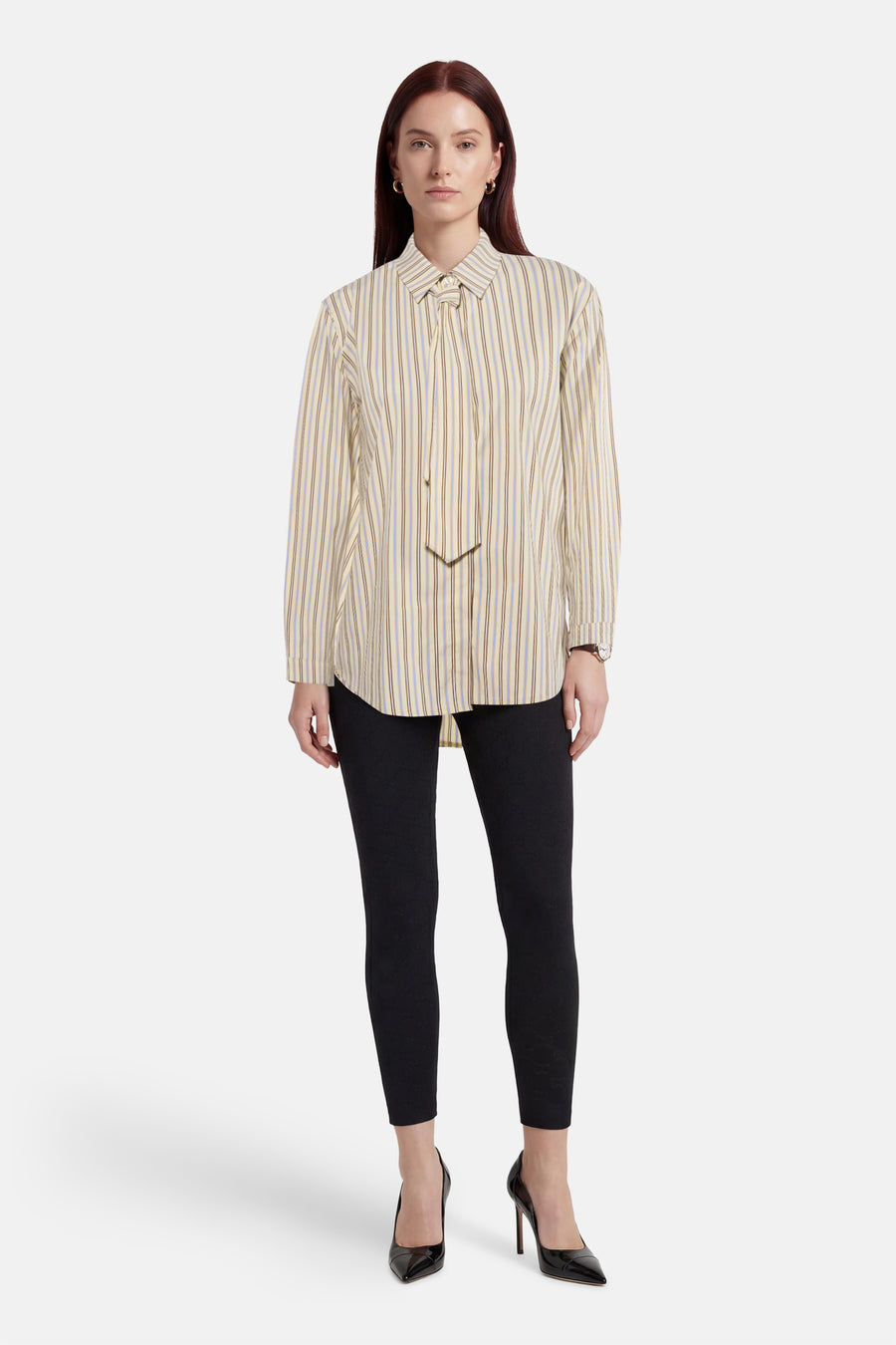 Geel gestreept overhemd van Terra di Siena, met lange mouwen en een knoopdetail bij de hals, gedragen met zwarte leggings en hakken.
