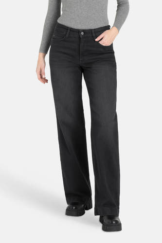 Jean boyfriend noir de MAC, avec une main dans la poche et associé à un pull gris et des chaussures noires.