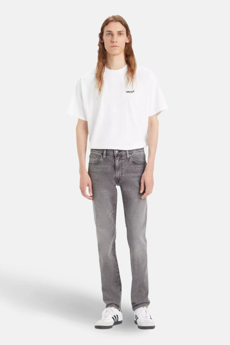 Man in witte T-shirt, grijze jeans en Adidas sneakers.
