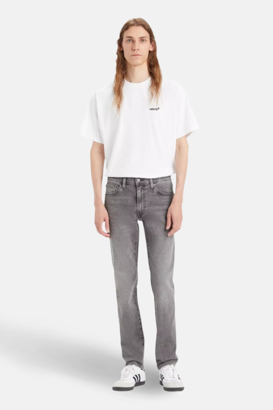 Jean slim fit léger gris de Levi's, porté avec un t-shirt blanc et des baskets blanches à rayures noires.