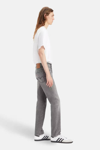 Jean slim fit gris de Levi's, porté avec un T-shirt blanc et des baskets blanches, en vue latérale.