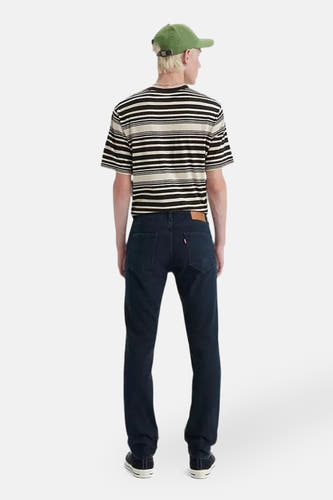 Jean slim bleu marine denim de Levi's, vu de de dos, avec un t-shirt rayé et une casquette verte.
