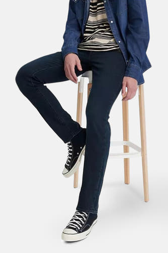 Jean slim de denim bleu foncé de Levi's®, porté avec un haut rayé et une chemise en denim, assis sur une chaise roulante.