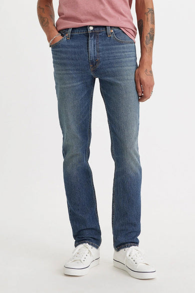 Jean slim-fit bleu moyen de Levi's®, profil latéral, avec délavage léger et poches classiques, porté avec un t-shirt rose et des baskets blanches.