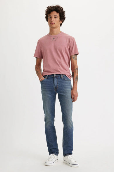 Jean slim-fit bleu moyen de Levi's® avec délavage clair, porté avec un t-shirt rose et des baskets blanches, vue de face