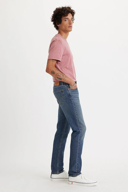 Mid blue slim-fit jeans van Levi's®, zijprofiel, met lichte slijtage en klassieke zakken, gedragen met roze t-shirt en witte sneakers.