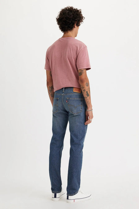 Jean slim-fit bleu moyen de Levi's® avec délavage délavé, poches arrière et fermeture éclair, vu de dos sur mannequin portant un t-shirt rose et des baskets blanches.