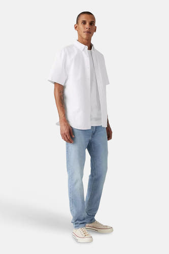 Jeans slim fit de Levi's®, en denim bleu clair, combiné avec des baskets blanches et une chemise blanche.
