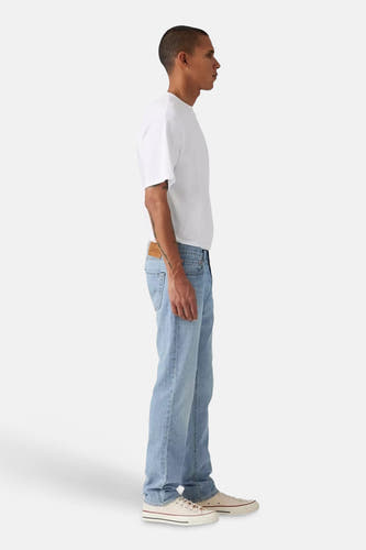 Jean slim bleu clair de Levi's, vu de côté, associé à un t-shirt blanc et des baskets de couleur crème.