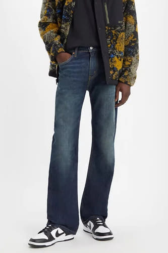 Jean bootcut en denim de Levi's, avec un délavage bleu classique, combiné avec un t-shirt noir et des baskets noires et blanches.