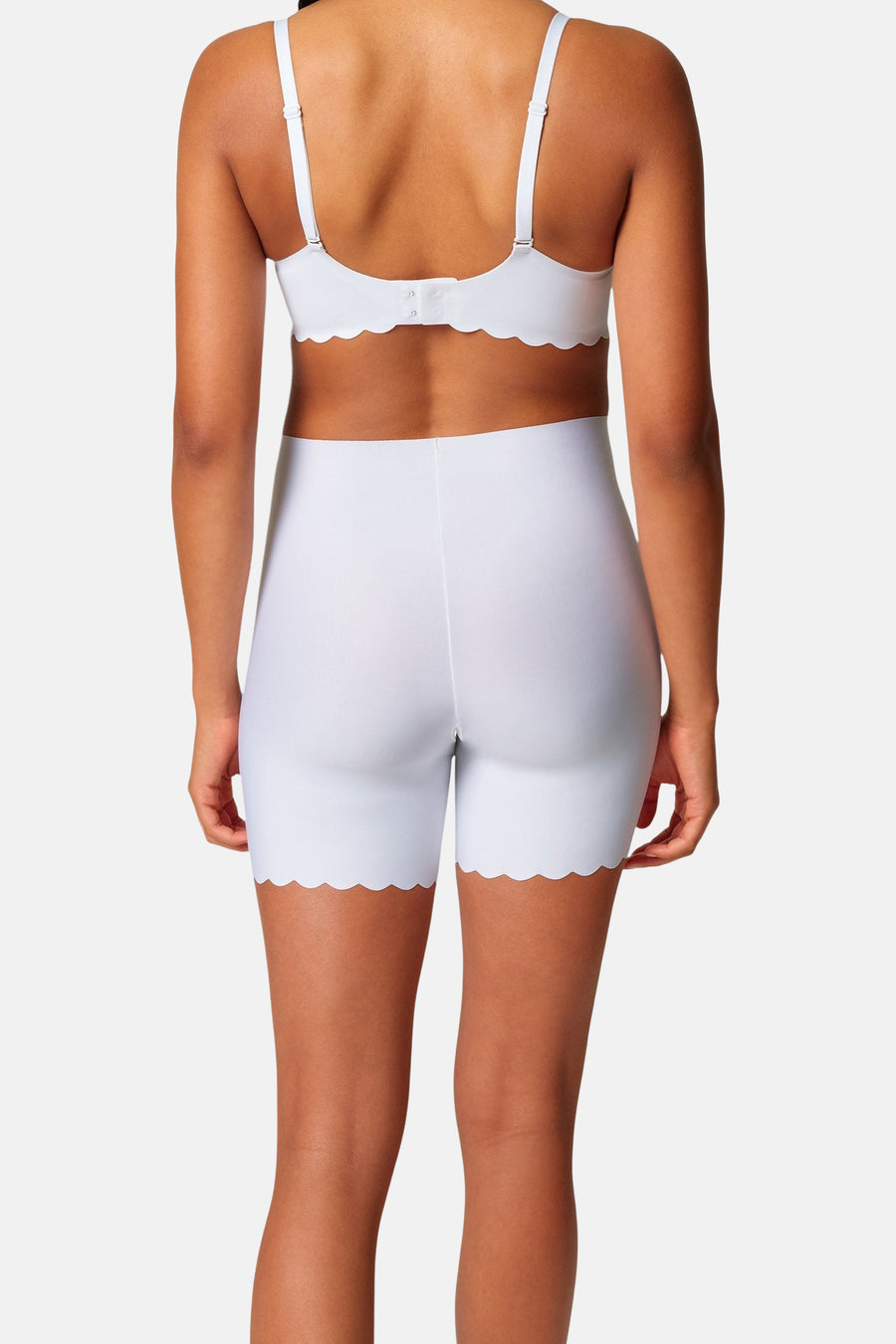 Witte shorty van SKINY, achterkant gezien, met een geschulpte zoom en een witte bh.
