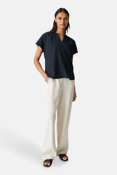 Blouse bleue marine à manches courtes d'OPUS, portée avec un pantalon beige et des sandales noires.