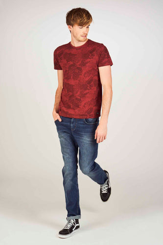 Man in rode T-shirt, blauwe jeans en zwarte sneakers.