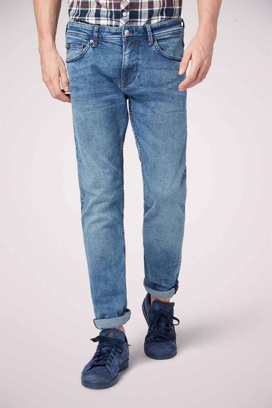 Staande man in blauwe jeans en suède schoenen.