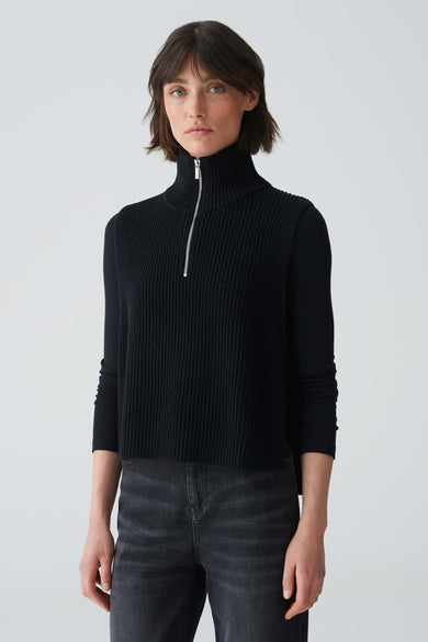 Chapeau noir d'OPUS, avec une texture à larges rayures et porté avec un manteau noir et des jeans gris en vue de côté.