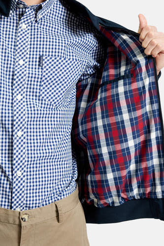 Veste courte bleue de BEN SHERMAN avec doublure à carreaux, portée sur une chemise à carreaux bleu et blanc et un pantalon kaki.