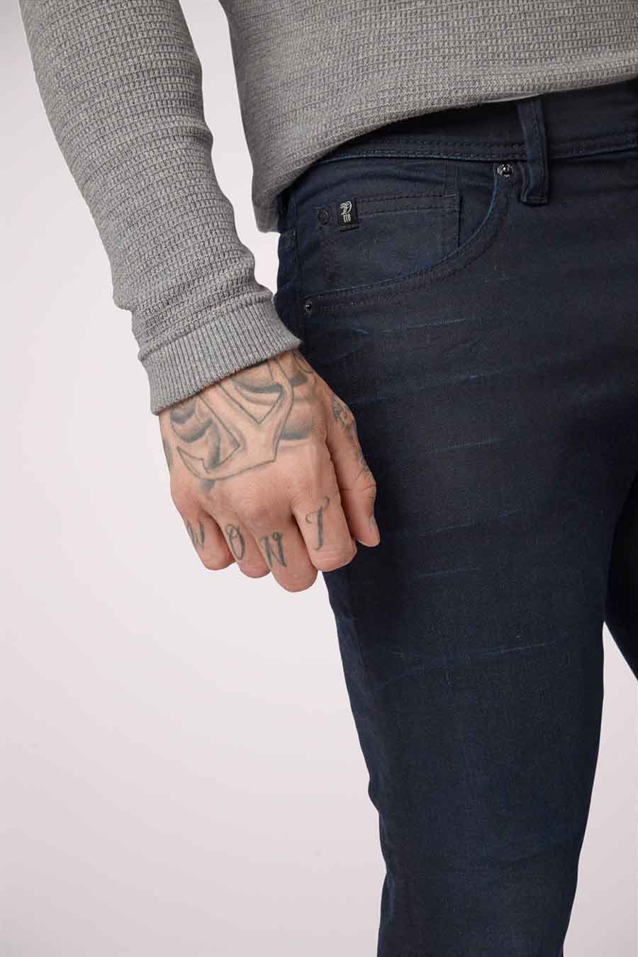 Jean slim fit bleu marine en denim de TOM TAILOR, avec des tatouages sur la main, et une chemise grise.