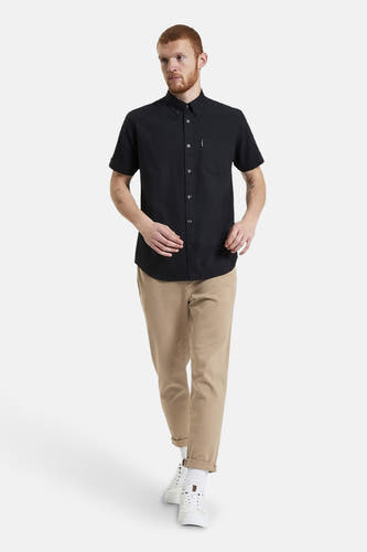 Chemise noire à manches courtes de BEN SHERMAN, avec poche poitrine, portée avec un pantalon kaki et des baskets blanches.