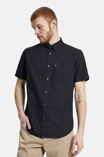 Chemise noire à manches courtes de Ben Sherman, avec poche poitrine et portée avec un pantalon beige.