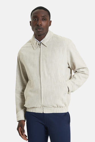 Manteau court beige de BEN SHERMAN, avec des manches longues et un élastique, porté avec un pantalon bleu marine.