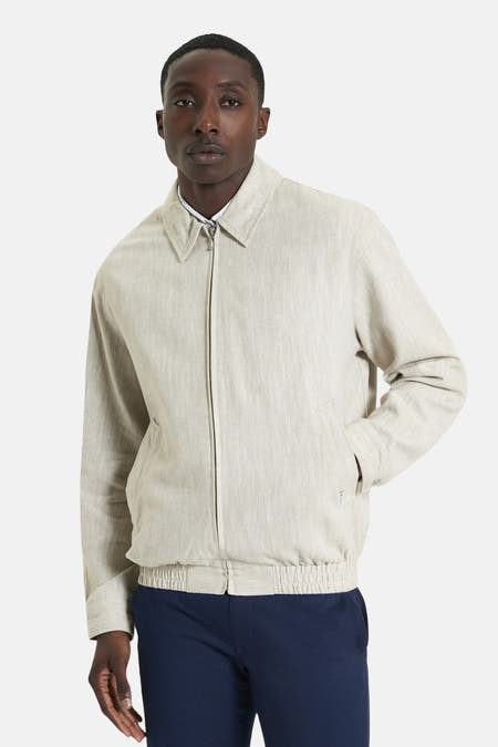 Manteau court beige de BEN SHERMAN, avec des manches longues et un élastique, porté avec un pantalon bleu marine.
