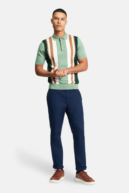 Veelkleurige polo van BEN SHERMAN, met verticale strepen en gedragen met een donkerblauwe broek en bruine schoenen.