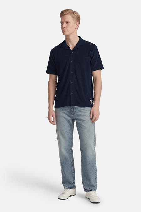Chemise bleue à manches courtes de BEN SHERMAN, portée avec un jean et des baskets blanches.