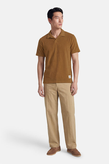 Bruine polo van BEN SHERMAN, met korte mouwen en een vintage kraag, gecombineerd met beige gestreepte pantalon en bruine loafers.